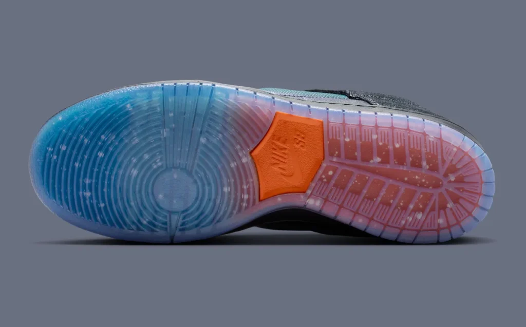 Outsole view of the Bluetile x Nike SB Dunk Low “Monarch Butterfly” showcasing a translucent rubber sole with blue-to-orange sunset gradients, white speckled detailing, and an orange Nike SB pivot section at the midfoot
