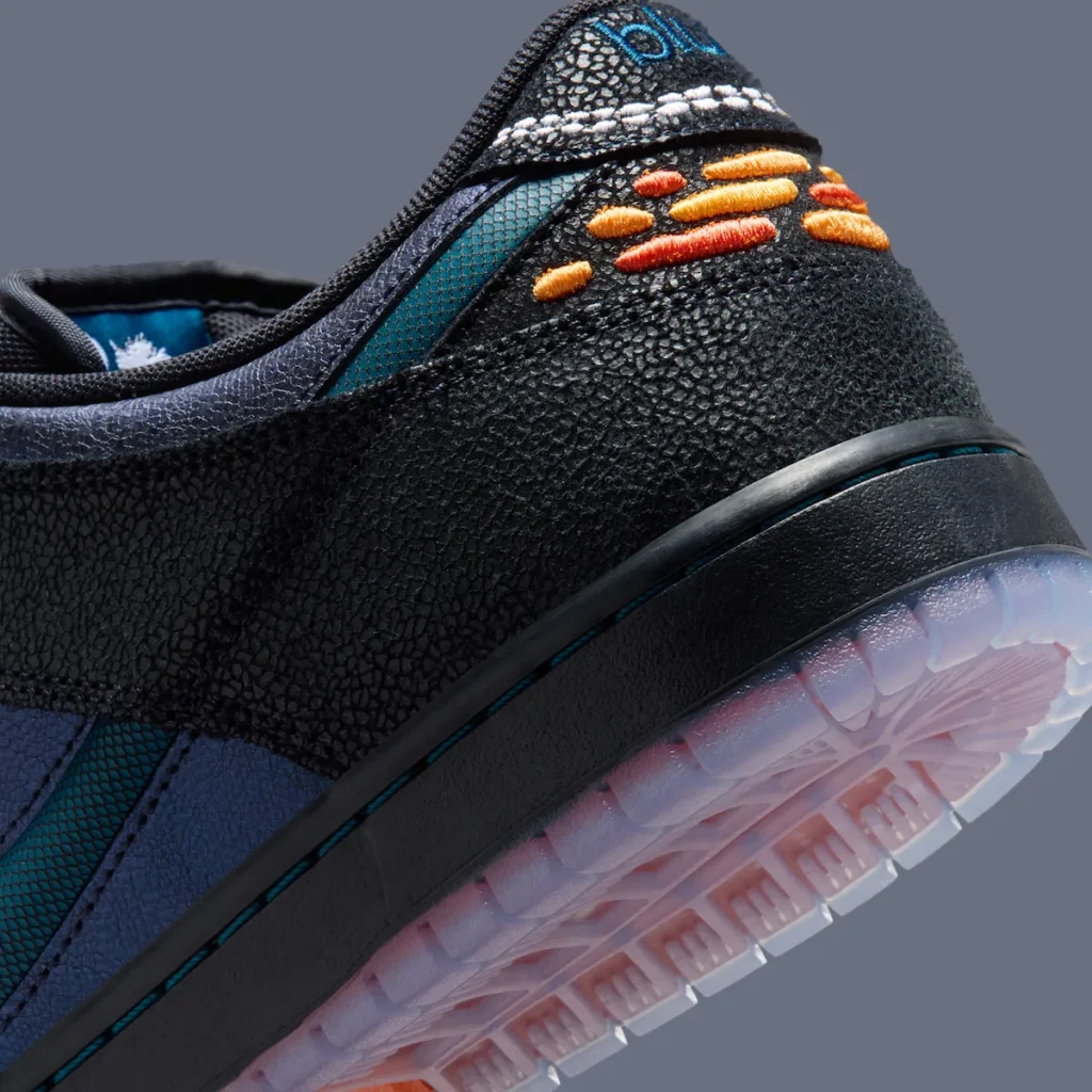 Close-up heel detail of the Bluetile x Nike SB Dunk Low “Monarch Butterfly” featuring cracked black textured overlays, embroidered orange monarch-inspired wing graphics, split Bluetile branding on the heel tab, and a translucent outsole with soft sunset gradient tones
