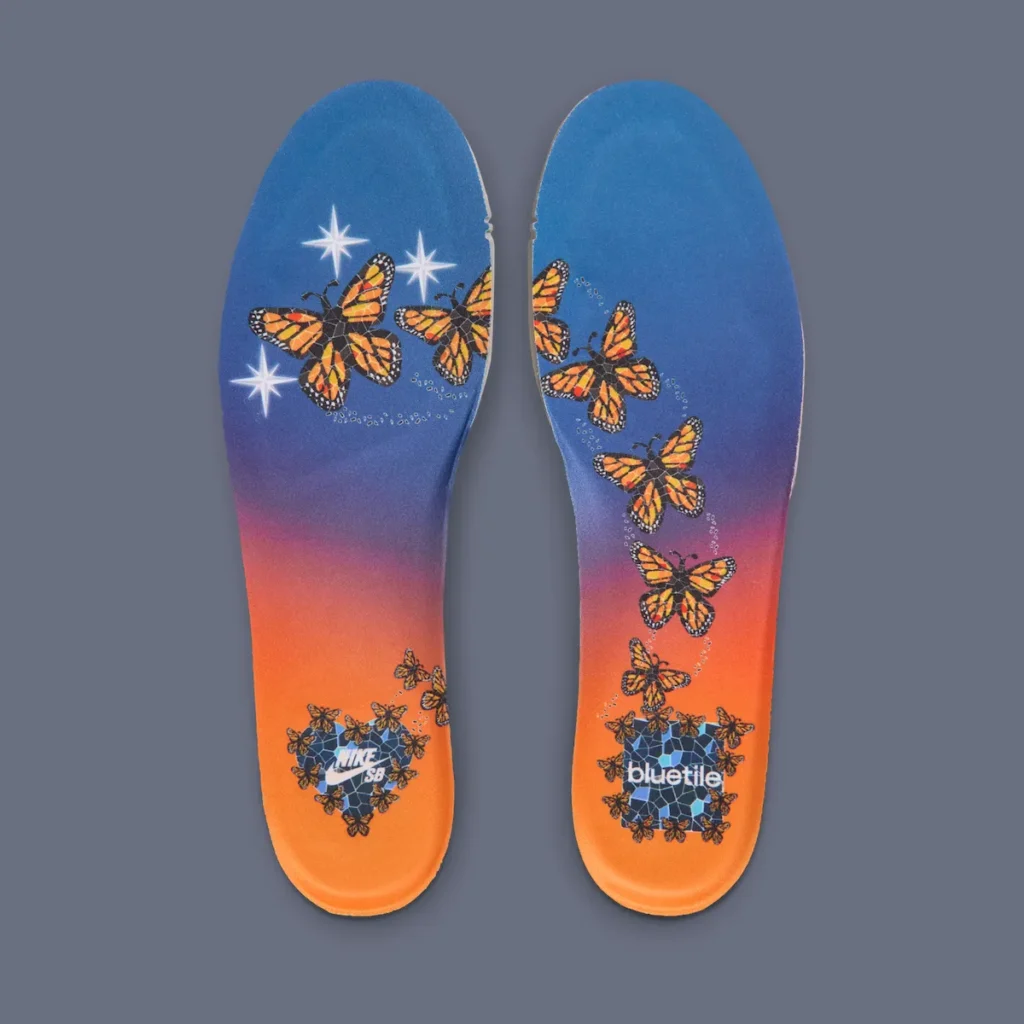 Custom insoles from the Bluetile x Nike SB Dunk Low “Monarch Butterfly” featuring vibrant blue-to-orange sunset gradients, flying monarch butterfly graphics, sparkling star details, and co-branded Nike SB and Bluetile artwork near the heel
