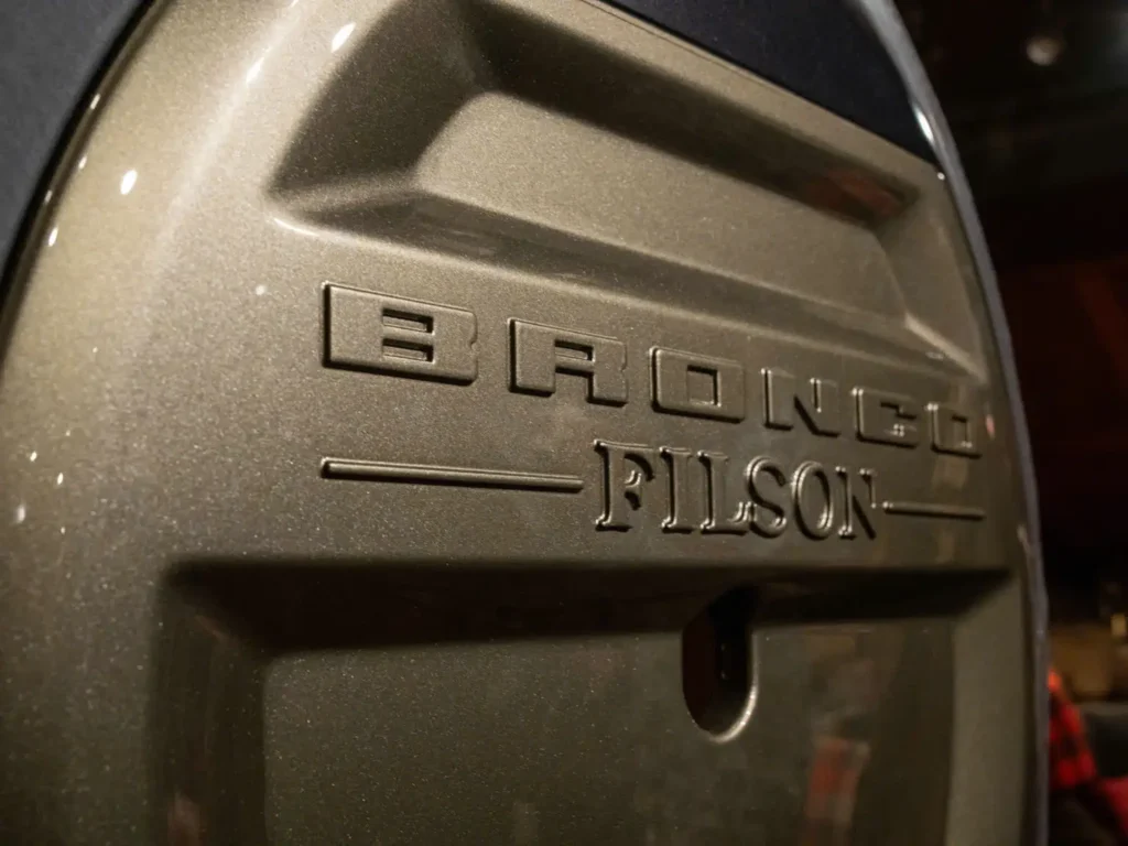 Close-up detail of a Ford Bronco tailgate featuring embossed “BRONCO FILSON” badging in a metallic finish, highlighting the rugged collaboration branding and textured exterior surface