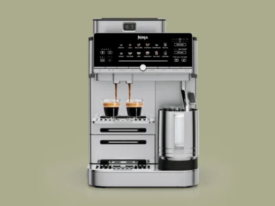 Ninja AutoBarista Pro fully automatic espresso machine in stainless steel finish brewing two espresso shots into double-wall glass cups, featuring a touchscreen interface, dual bean hopper system, and integrated milk frothing pitcher