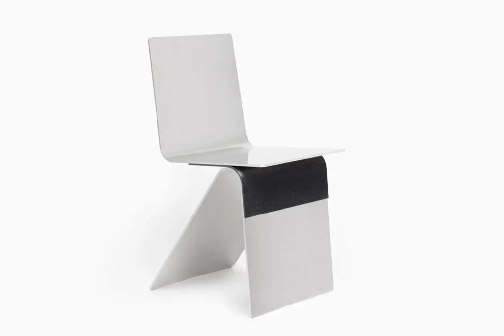 Studio product shot of a minimalist sculptural chair made from folded brushed aluminum, featuring geometric architectural lines, curved industrial detailing, and a monochrome metallic finish against a clean neutral background