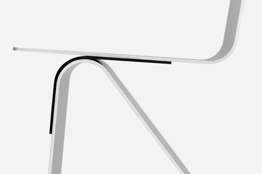 Minimalist close-up of a sculptural brushed aluminum furniture design featuring sharp folded geometry, smooth curved transitions, and an industrial monochrome aesthetic against a clean studio backdrop