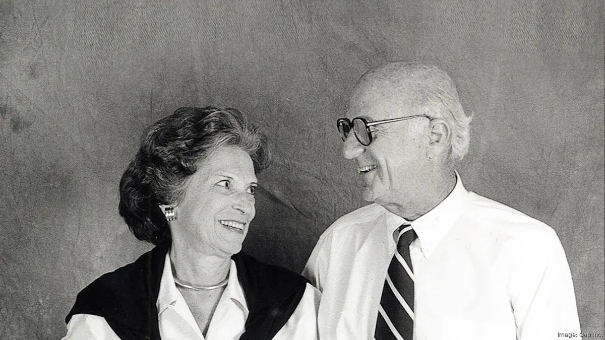 A black-and-white archival portrait of Doris and Don Fisher sharing a candid smile together, capturing the partnership that helped build Gap Inc. into one of America’s most influential retail companies. Dressed in understated business attire, the couple’s warm expression and relaxed posture reflect the collaborative spirit, quiet ambition, and personal chemistry that defined their decades-long impact on fashion, philanthropy, and the cultural identity of San Francisco