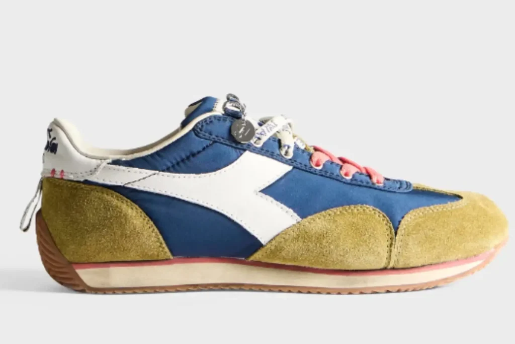 This JW Anderson x Diadora Equipe colorway combines deep navy nylon with mustard suede overlays, white leather side stripes, and soft pink laces for a playful reinterpretation of the archival runner. The slim silhouette and vintage-inspired sole preserve the Equipe’s 1975 athletic identity, while the bold color contrasts and premium Italian materials push it firmly into contemporary luxury sneaker territory