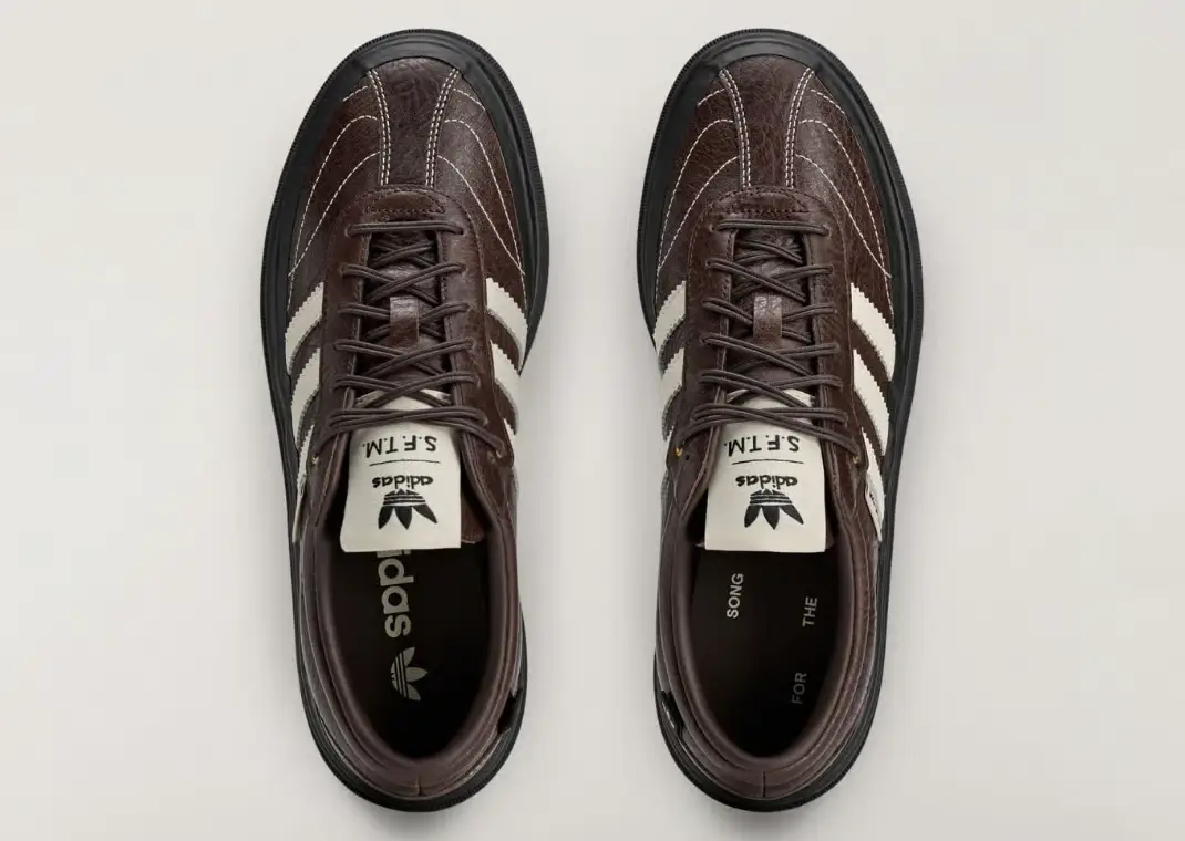 A top-down product shot of the Song For The Mute x adidas Samba LX Freizeit in the “Aurora Coffee” colorway highlights the pair’s deep brown tumbled leather upper, contrast white stitching, cream Three Stripes, and thick black lugged sole. Co-branded tongue tags and minimalist interior branding reinforce the collaboration’s understated haute and worn-in aesthetic