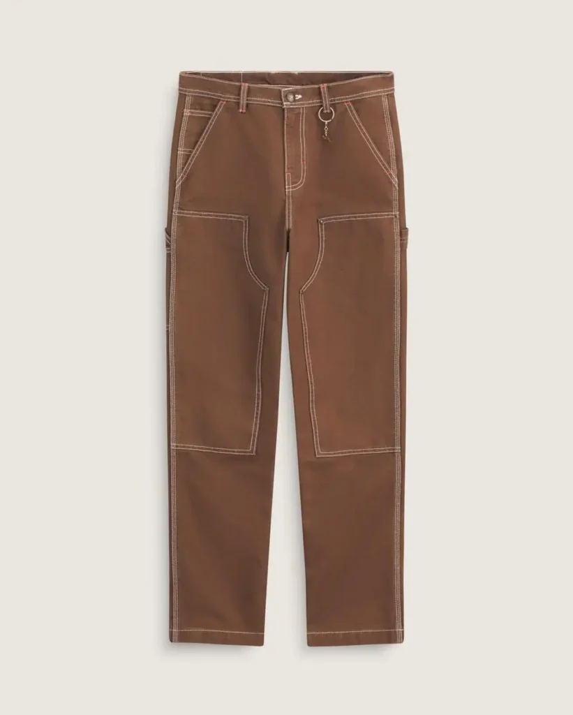 Brown carpenter-style work pants featuring contrast white stitching, reinforced utility panel construction, relaxed straight-leg tailoring, and a small metallic charm detail attached near the waistband against a clean neutral background