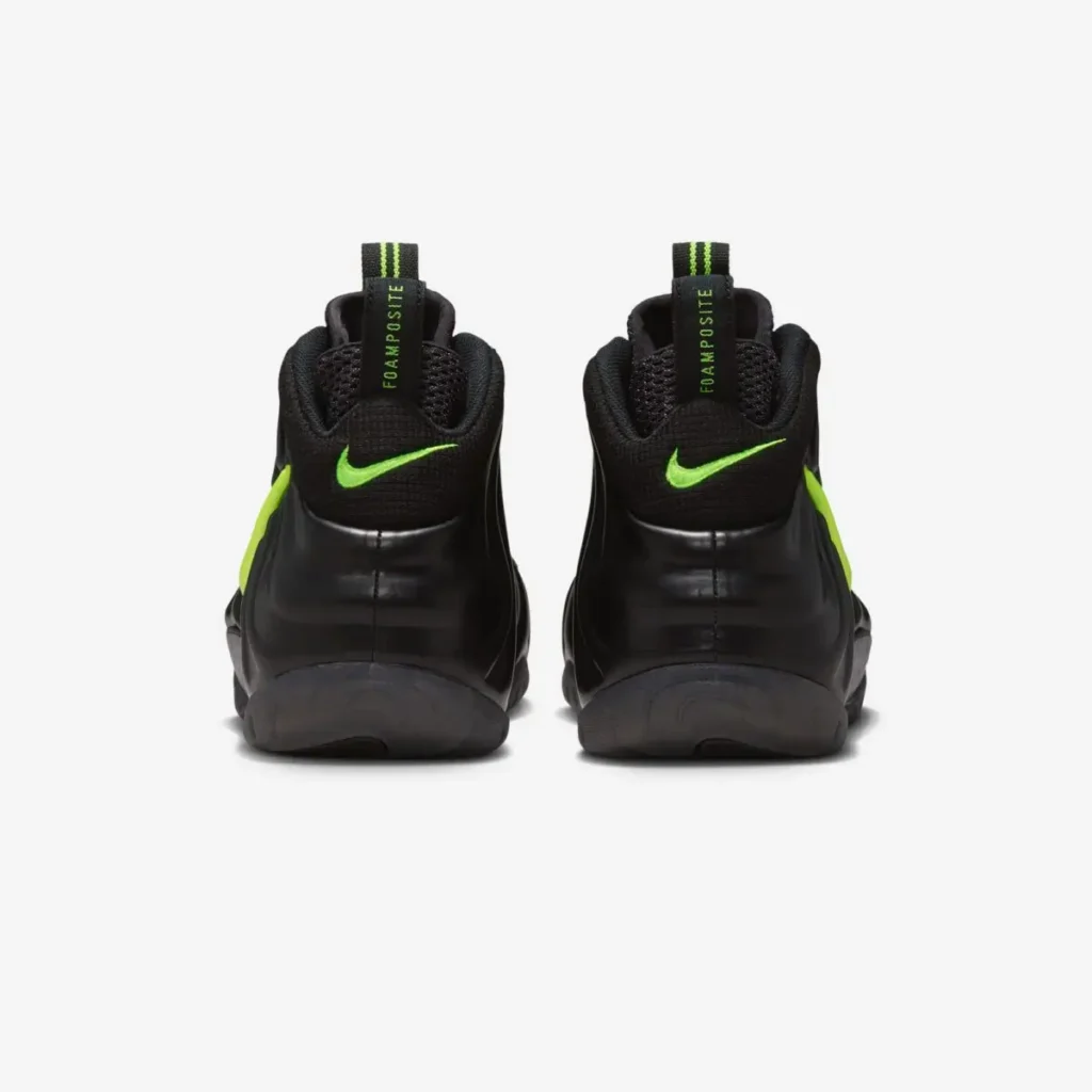 Rear view of the Nike Air Foamposite Pro “Voltage,” showing the glossy black molded shell wrapping the heel, neon Voltage Yellow mini Swooshes on each back panel, vertical heel pull tabs with striped detailing and “FOAMPOSITE” text, and a smoky translucent outsole at the base