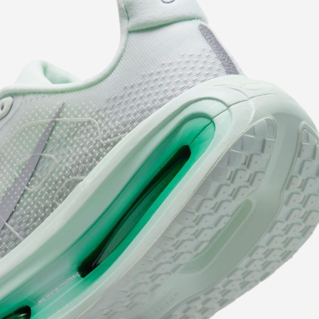 Close-up of the Nike Vomero Premium Women’s “Barely Green” (HM5973-300) heel and midsole, emphasizing the sculpted foam sidewall, translucent green-tinted Air Zoom cushioning unit, and the textured outsole edge with a grid traction pattern, alongside the subtle metallic silver Swoosh on the upper