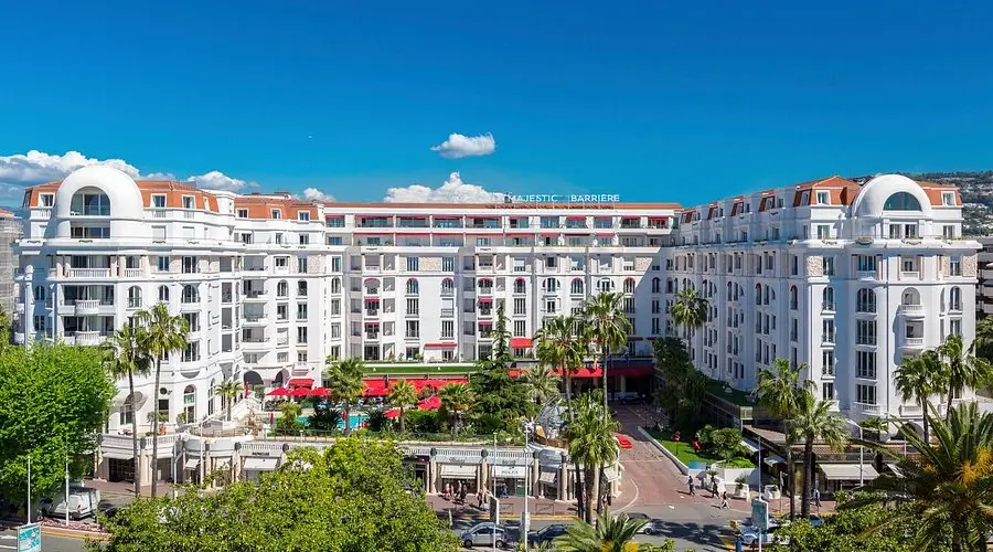 Hôtel Barrière Le Majestic captures the timeless glamour of the French Riviera through its expansive white façade, palm-lined entrance, and refined Mediterranean architecture. Closely tied to the atmosphere of the Cannes Film Festival, the hotel projects a balance of cinematic prestige and resort-style relaxation. Curved rooftop detailing, symmetrical balconies, and lush central gardens create a polished yet inviting atmosphere, while the bright Riviera sky enhances the property’s luxurious coastal identity. More than a hotel, the space feels like a self-contained lifestyle destination where hospitality, fashion, and cultural spectacle naturally intersect