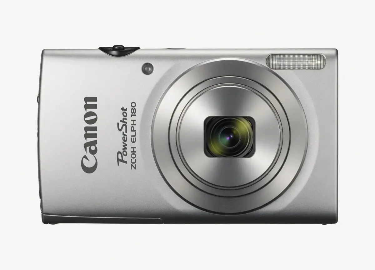 A clean studio product image of the silver Canon PowerShot ELPH 180 compact digital camera photographed against a light gray background. The front-facing composition highlights the circular zoom lens, integrated flash, minimalist metallic body, and classic point-and-shoot design that has become synonymous with the modern digicam revival trend