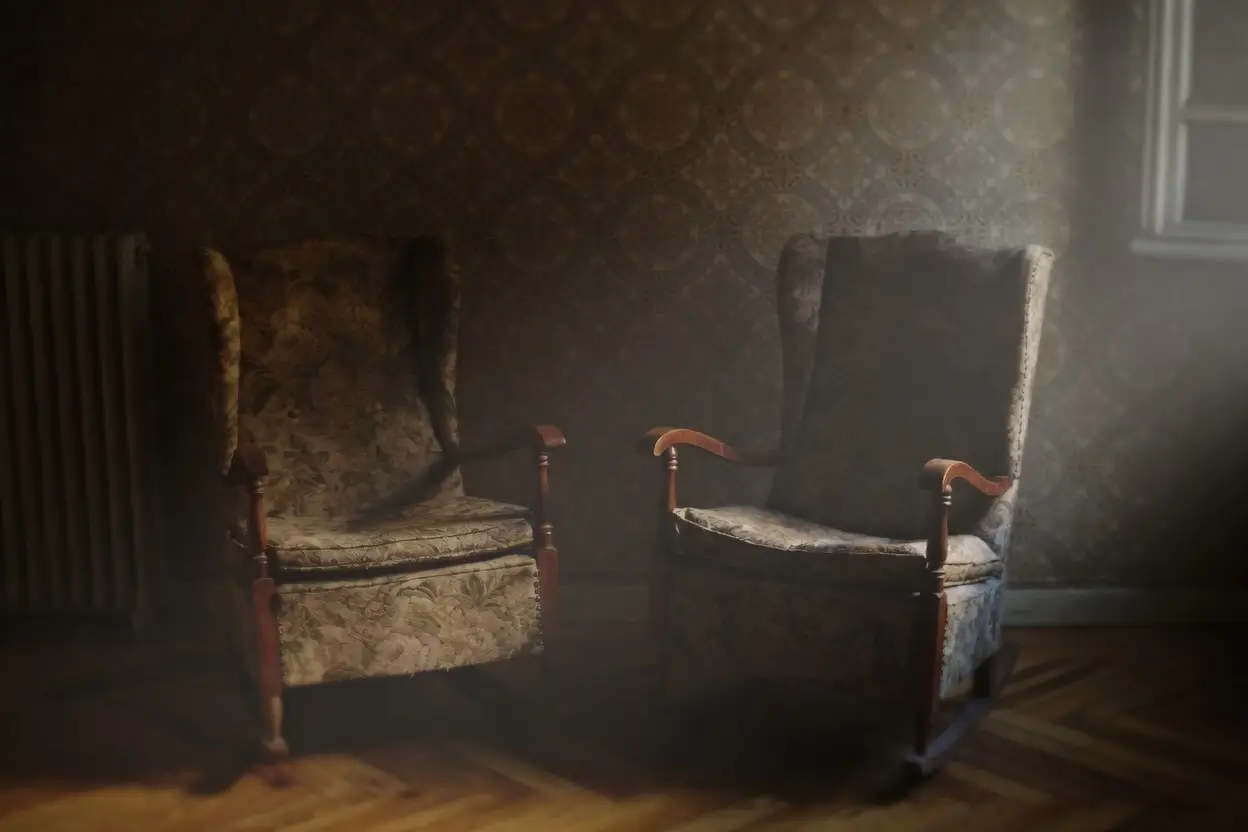 Two vintage upholstered wingback armchairs sit side by side inside a dimly lit room washed in warm, cinematic haze. Patterned wallpaper and aged wooden flooring reinforce the atmosphere of an old interior frozen in time, while soft daylight filters through a nearby window, casting muted shadows across the chairs and floorboards. The scene carries a melancholic, almost spectral stillness, balancing domestic comfort with an eerie sense of abandonment and memory