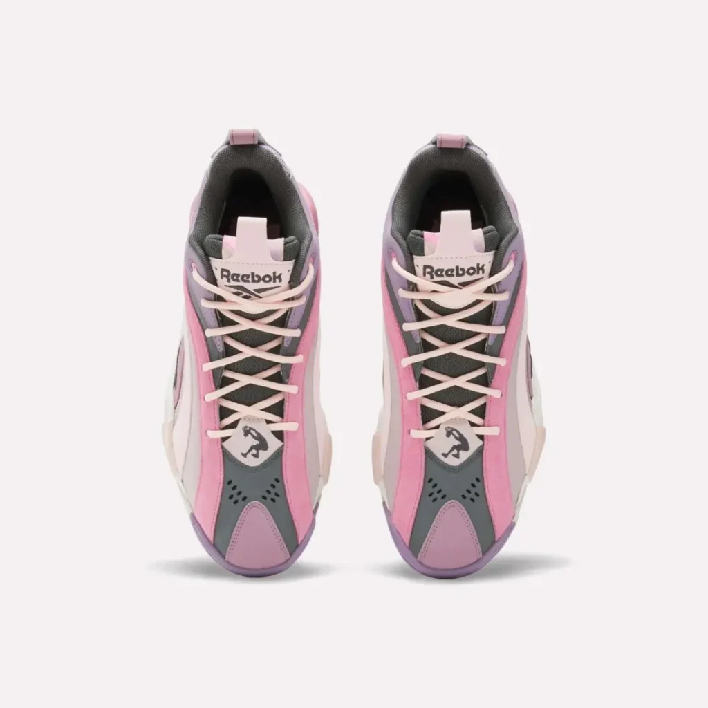 Top-down view of pastel Reebok basketball sneakers with pink suede overlays, lavender toe accents, charcoal mesh tongues, and cream laces on a light gray background