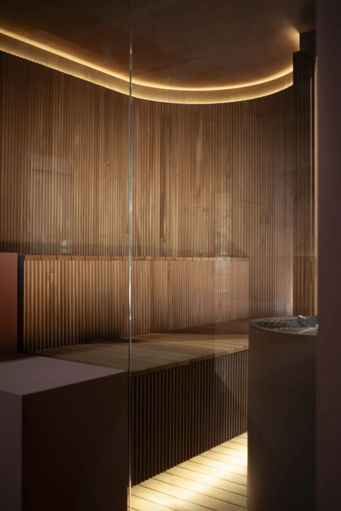 Warmly lit interior of the Baluar sauna by Patricia Urquiola for Effe, featuring ribbed wood walls, curved ceiling lighting, and minimalist bench seating