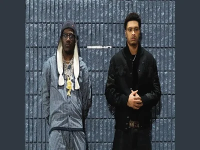 Nemzzz and Lil Yachty stand against a textured concrete block wall in a stark nighttime setting, reinforcing the cold, minimalist aesthetic surrounding “GEEKIN.” Yachty appears layered in oversized monochrome streetwear with stacked chains, a knit cap, and glasses, bringing his eccentric Atlanta energy into the frame, while Nemzzz contrasts him with a more restrained all-black look featuring a varsity-style jacket and dark denim. The muted palette, rigid composition, and industrial backdrop mirror the hypnotic, skeletal atmosphere of the single itself, emphasizing tension between chaos and composure within the Manchester-Atlanta