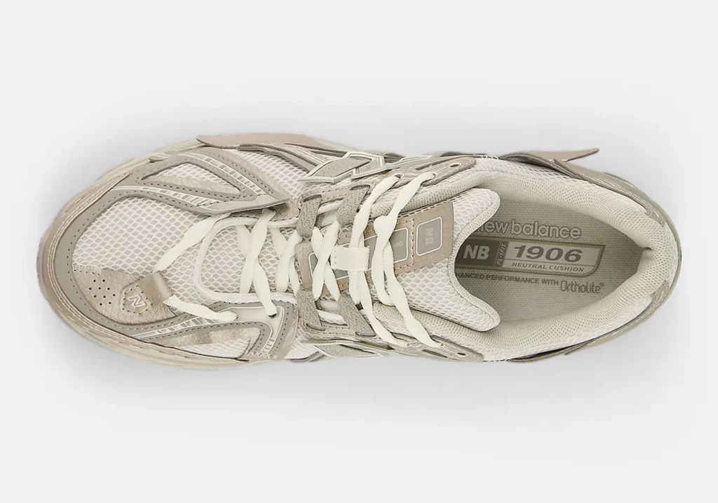 Top-down view of the New Balance 1906A “Arid Stone” featuring layered cream mesh, sandy synthetic overlays, asymmetrical deconstructed detailing, and tonal laces with subtle metallic accents across the technical runner silhouette