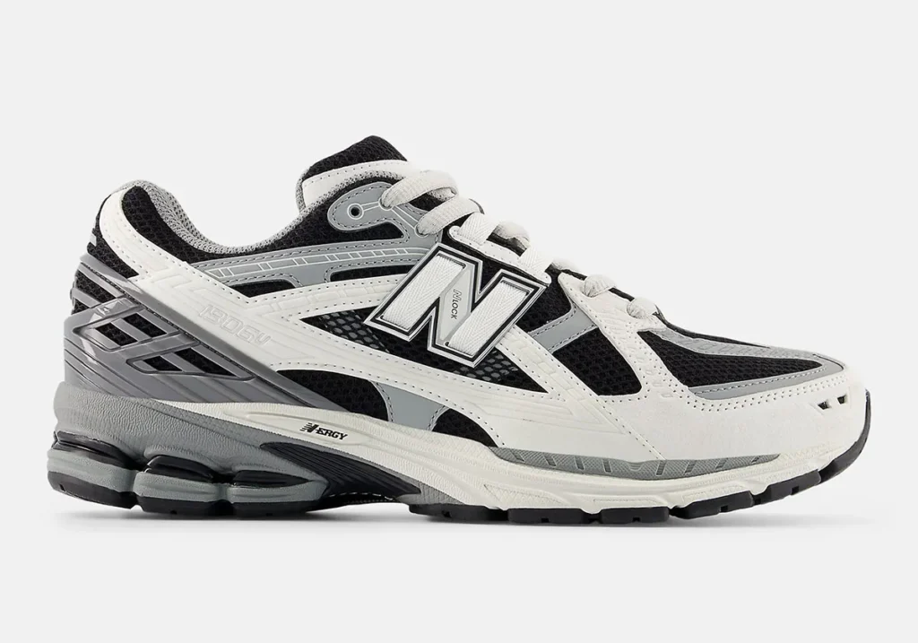 Angled side view of the New Balance 1906 in a black, white, and grey colorway featuring breathable black mesh underlays, layered white synthetic paneling, and metallic grey support accents around the heel and midfoot. The oversized outlined “N” logo dominates the sidewall, while sculpted ABZORB cushioning pods and view stability components reinforce the shoe retro performance-runner identity. Technical overlays, segmented tooling, and textured midsoles combine to give the silhouette a layered early-2000s running aesthetic with modern streetwear appeal