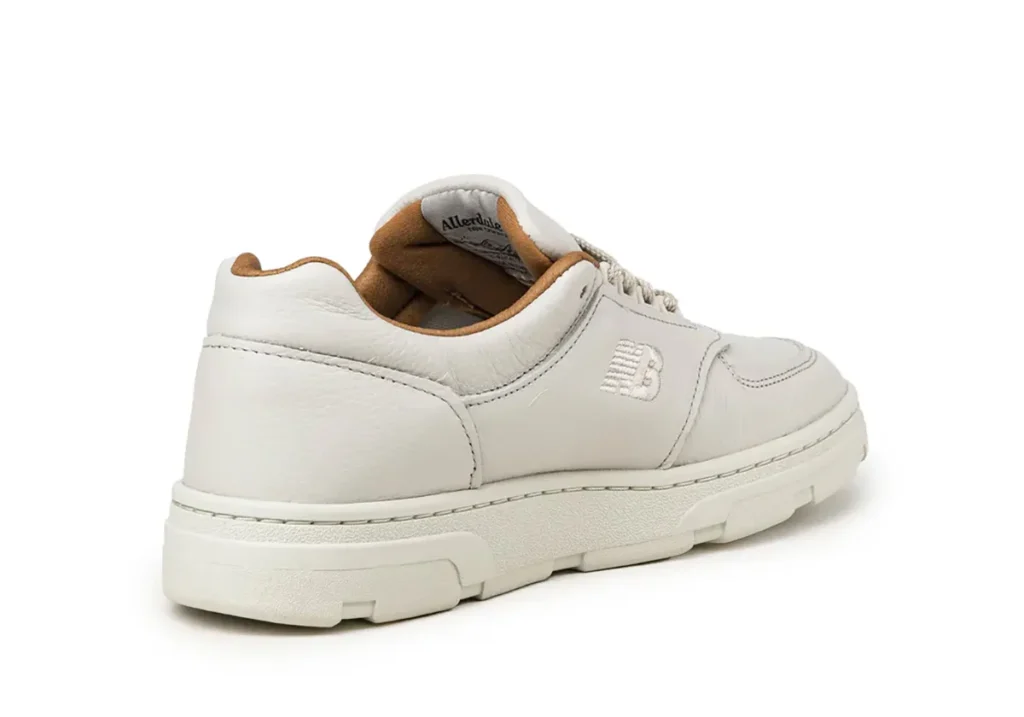 Rear-angle product shot of the New Balance Allerdale shoe in Vaporous Grey and Chipmunk, featuring premium off-white leather panels, tonal embroidered “NB” branding, cream rubber tooling, and a soft tan interior lining against a clean studio backdrop