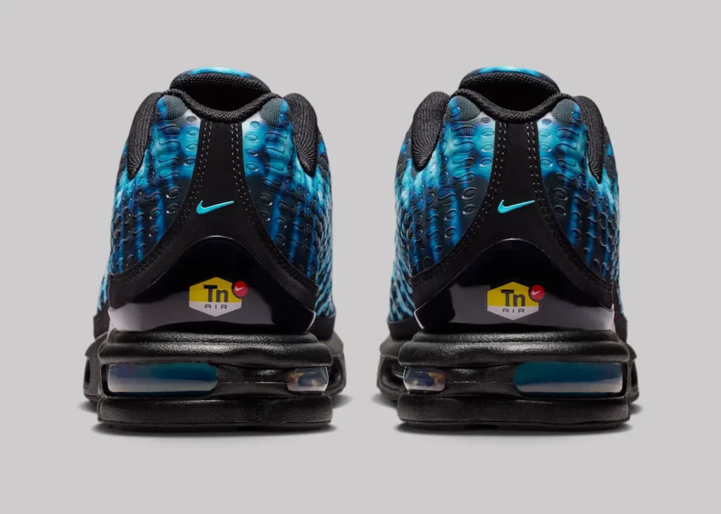 Rear view of Nike Air Max Plus VII “Scorpion” shoe showing black heel counter with mini blue Swoosh, TN Air logo badge in yellow and red, blue gradient textured upper, and visible Tuned Air cushioning units in the heel