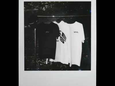 Black-and-white campaign image showing Nike BTS apparel hanging on a clothing rack, including graphic T-shirts, a hoodie, and a cap in a moody studio set
