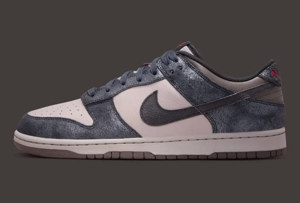 Lateral profile view of the Nike Dunk Low “CBGB” featuring distressed charcoal-grey overlays with a weathered, almost ash-like texture layered against muted off-white leather underlays. A cracked black leather Swoosh stretches across the sidewall while tonal laces, an aged-look midsole, and subtle red heel embroidery complete the shoe understated tribute to New York’s legendary punk venue and its raw downtown aesthetic