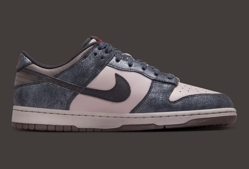 Side profile of the Nike Dunk Low “CBGB” showcasing distressed charcoal-grey overlays layered over muted off-white leather panels. The shoe features a textured black Swoosh, tonal laces, aged-look midsole, and subtle red accents at the heel and tongue, translating the worn, underground atmosphere associated with New York’s iconic CBGB era into a refined shoe silhouette