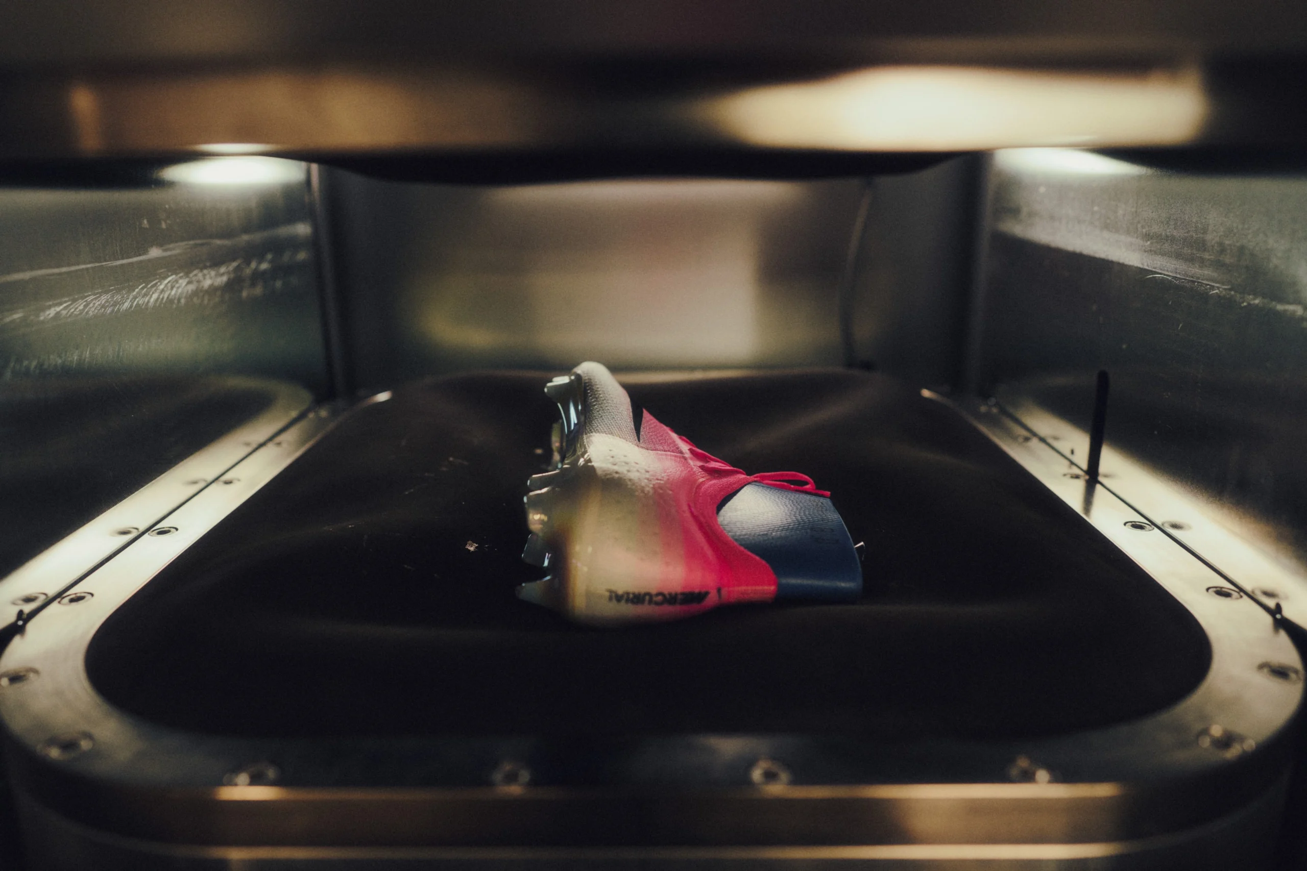 Nike Mercurial football boot positioned inside a testing and shaping chamber, highlighting the precision manufacturing process and performance engineering