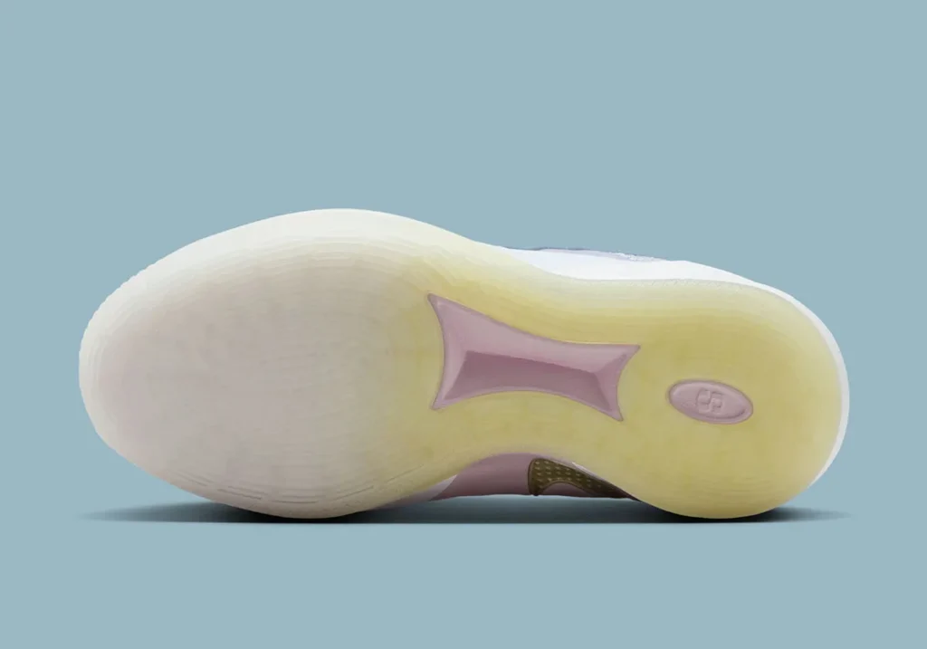 Outsole view of the Nike Sabrina 3 “Football Grey / Royal Pulse,” showcasing a translucent rubber sole with a soft yellow tint blending into milky white at the forefoot. The traction pattern features fine, radial and wave-like grooves for multi-directional grip, while a lilac-pink midfoot shank plate sits at the center for stability. A small circular Sabrina logo is embedded near the forefoot, with subtle texturing throughout, all set against a muted blue studio background