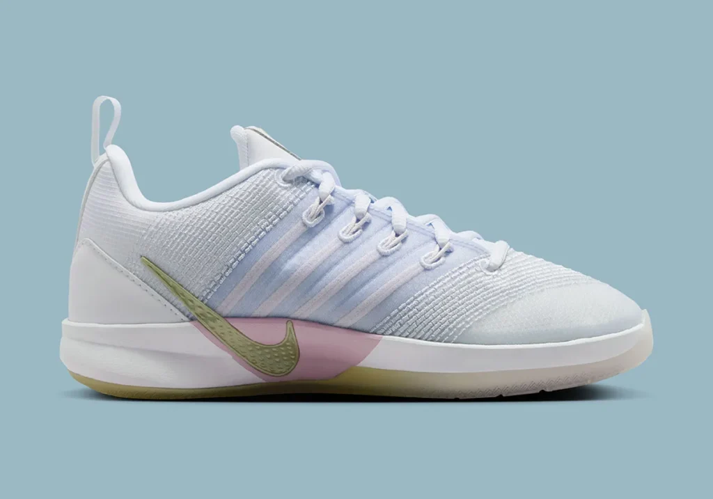 Medial side profile of the Nike Sabrina 3 “Football Grey / Royal Pulse,” featuring a soft white and light grey engineered mesh upper with subtle pastel blue and lilac striping through the midfoot. The lace system integrates into layered support bands, while a muted olive-toned mini Swoosh wraps low along the midsole above a pink foam segment. The heel includes a structured white counter with a pull tab, and the translucent outsole shows a faint yellow tint, all set against a muted blue studio backdrop