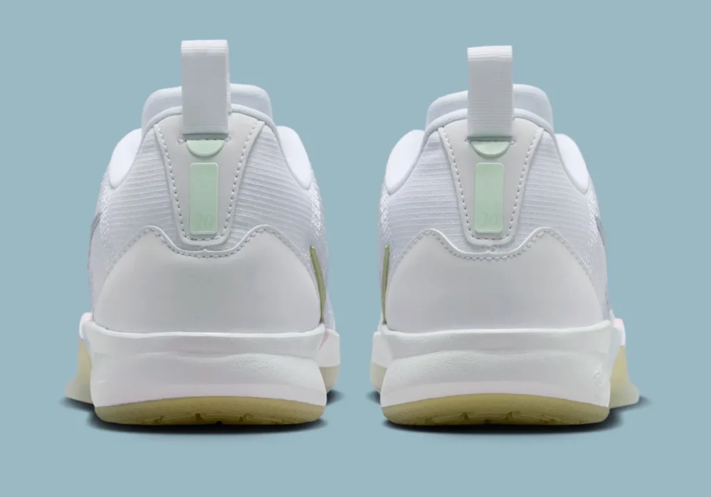 Rear heel view of the Nike Sabrina 3 “Football Grey / Royal Pulse,” showing a symmetrical pair with clean white heel counters and textured mesh uppers. Each heel features a vertical pull tab and a soft mint-green insert panel with subtle numbering detail, adding a minimal accent to the otherwise neutral palette. The midsole remains white with a slightly sculpted form, while the outsole reveals a faint translucent yellow tint at the base, all set against a muted blue studio background.