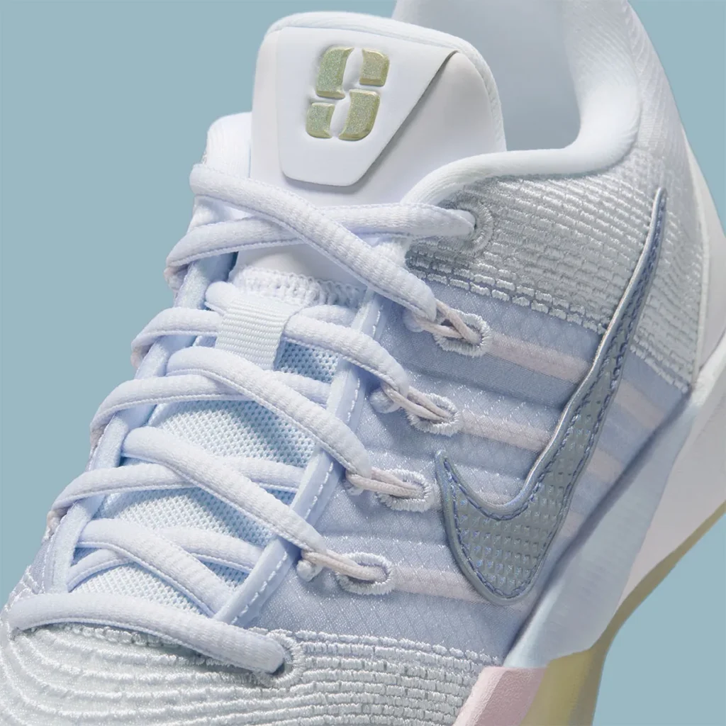 Close-up detail of the Nike Sabrina 3 “Football Grey / Royal Pulse,” focusing on the lacing system and midfoot structure. White laces thread through reinforced eyelets connected to translucent support bands, revealing soft pastel blue and lilac tones beneath the engineered mesh. A textured metallic Swoosh sits along the lateral side, while the tongue features a raised gold Sabrina logo. The layered materials and subtle sheen highlight the shoe’s balance of structure, breathability, and refined detailing