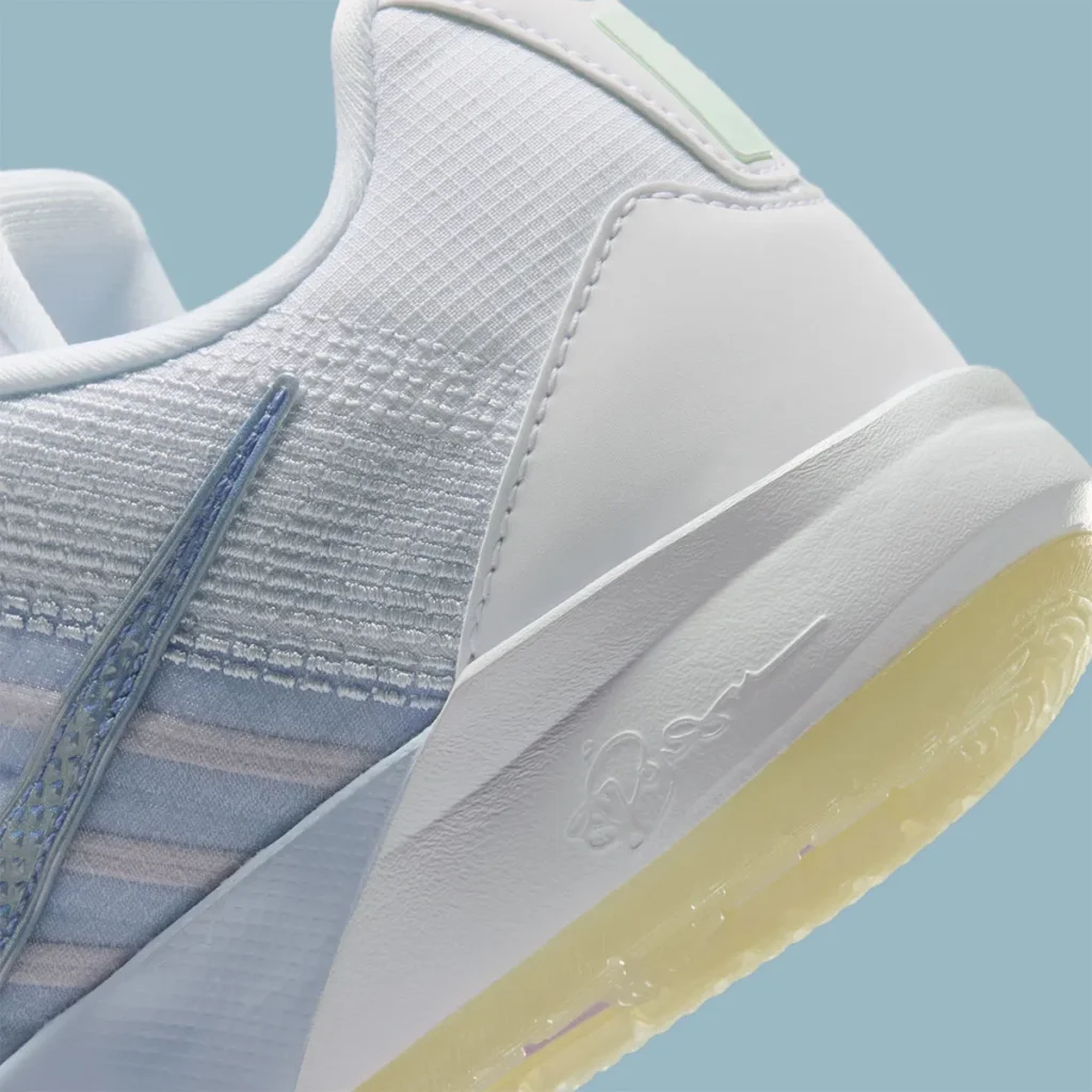 Close-up of the Nike Sabrina 3 “Football Grey / Royal Pulse” heel and midsole, highlighting the textured white heel counter and finely woven mesh upper with subtle pastel blue undertones. The metallic Swoosh edge is partially visible along the lateral side, while the midsole features a sculpted white foam wall stamped with Sabrina’s signature. Below, a translucent outsole with a soft yellow tint peeks through, emphasizing the shoe’s layered construction and clean, understated finish