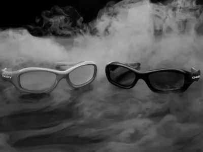 Two Oakley MUZM FatCat sunglasses in light and black colorways displayed in swirl smoke with sculpted wraparound frames and minimal studio lighting
