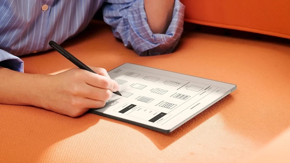 Person using a black stylus to write and organize templates on the reMarkable Paper Pure E Ink tablet while reclining on an orange sofa, highlighting the device’s paper-like digital workspace and minimalist interface