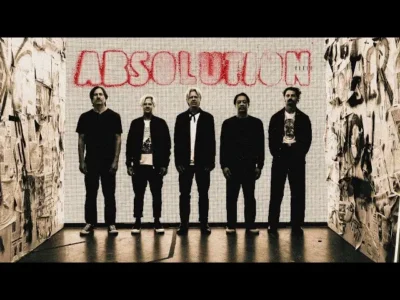 Switchfoot stand together in a narrow, collage-lined installation space beneath a large illuminated “ABSOLUTION” backdrop. The promotional image uses muted monochrome tones and dramatic contrast, emphasizing the band’s silhouette while reinforcing the reflective yet guitar-driven atmosphere of the single’s view identity
