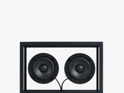 Front-facing view of the Transparent Sound Small Speaker in Black featuring dual exposed circular drivers, minimalist black aluminum framing, visible cabling, and industrial Scandinavian design against a clean gray background