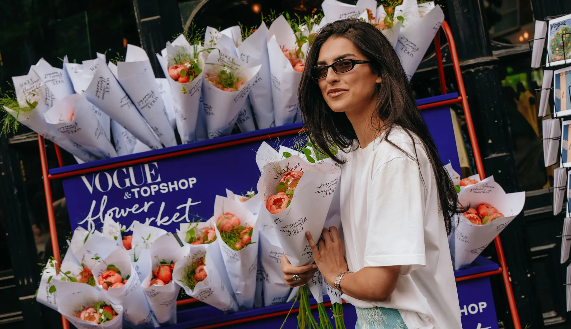 Woman holding wrapped flower bouquets in front of a Vogue & TOPSHOP Flower Market installation during the English Garden SS26 activation in Notting Hill