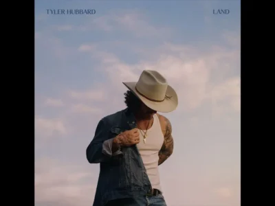 Cover artwork for “Land” by Tyler Hubbard featuring a solitary figure standing outdoors beneath a soft pastel sky. Wearing a cream cowboy hat, white tank top, open denim jacket, layered necklaces, and faded jeans, the subject looks downward with one hand adjusting the jacket. The minimalist composition and muted tones create a reflective, nostalgic country aesthetic. The text “TYLER HUBBARD” appears in the upper left and “LAND” in the upper right