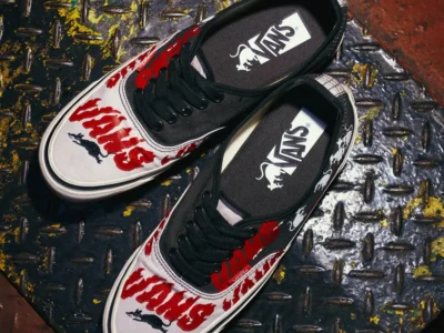 Editorial product image of the Vans x SOON.EASY Premium LX Authentic 44 photographed from above on a distressed industrial metal surface. The sneakers feature contrasting black and off-white canvas panels covered in oversized red hand-drawn typography, small cartoon character illustrations, and expressive graphic accents. Black laces and custom Vans-branded insoles complete the design, while the gritty setting reinforces the collaboration’s raw blend of skate heritage, underground art, and play social commentary
