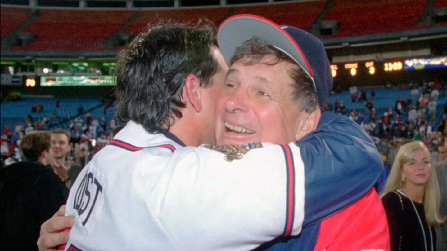 Bobby Cox embraces a player on the field following an Atlanta Braves victory, capturing the emotional warmth and fatherly leadership that defined his managerial career. Surrounded by stadium lights and celebrating fans, the moment reflects Cox’s deep bond with generations of Braves players