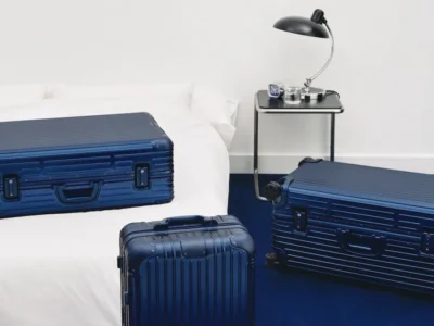 RIMOWA ORIGINAL luggage collection in new Ink Blue finish displayed in a minimalist hotel-inspired interior with aluminum suitcases on a bed and floor
