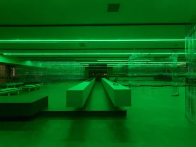 Interior view of H.Lorenzo’s new West Hollywood flagship illuminated in vivid green lighting, featuring sculptural metal display structures, minimalist furnishings, and an immersive futuristic retail environment