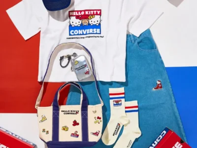 Flat lay of the Hello Kitty x Converse collection featuring a graphic T-shirt, denim skirt, canvas tote, socks, cap, pouch, and accessories arranged beside bright red Converse shoe boxes
