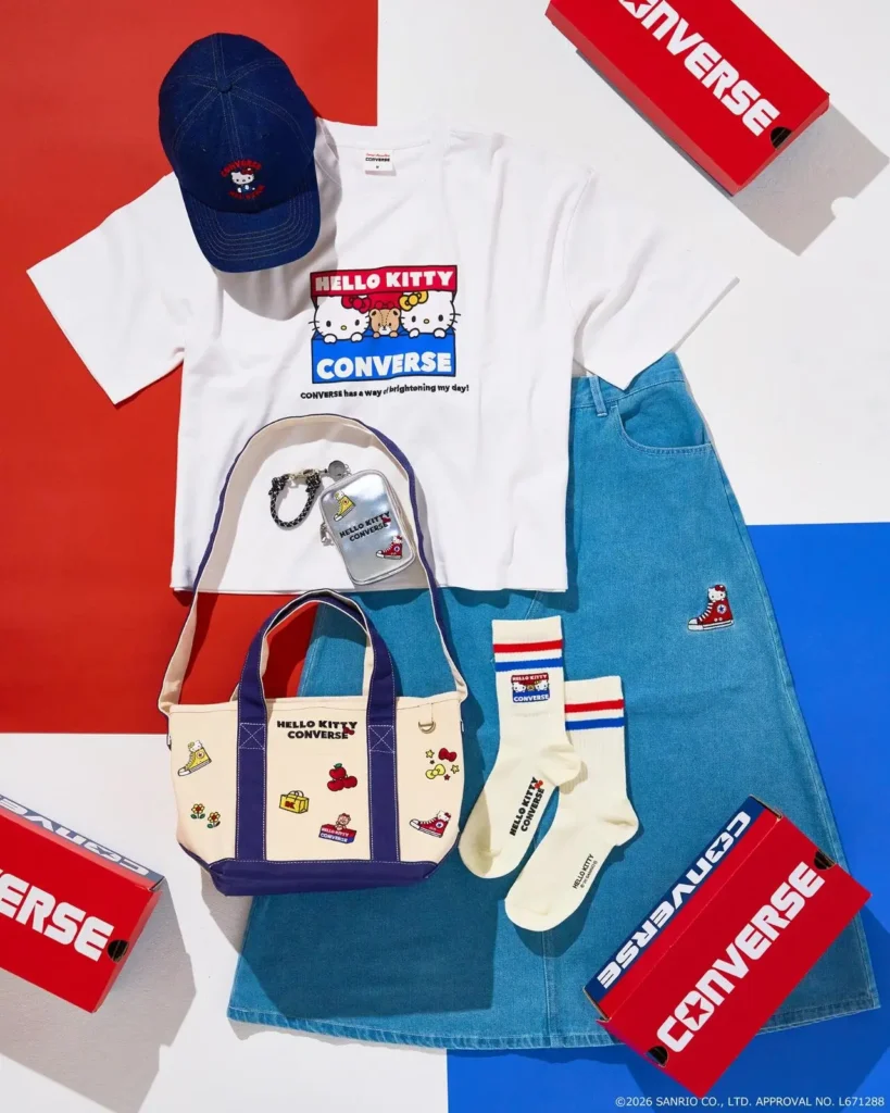 Flat lay of the Hello Kitty x Converse collection featuring a graphic T-shirt, denim skirt, canvas tote, socks, cap, pouch, and accessories arranged beside bright red Converse shoe boxes