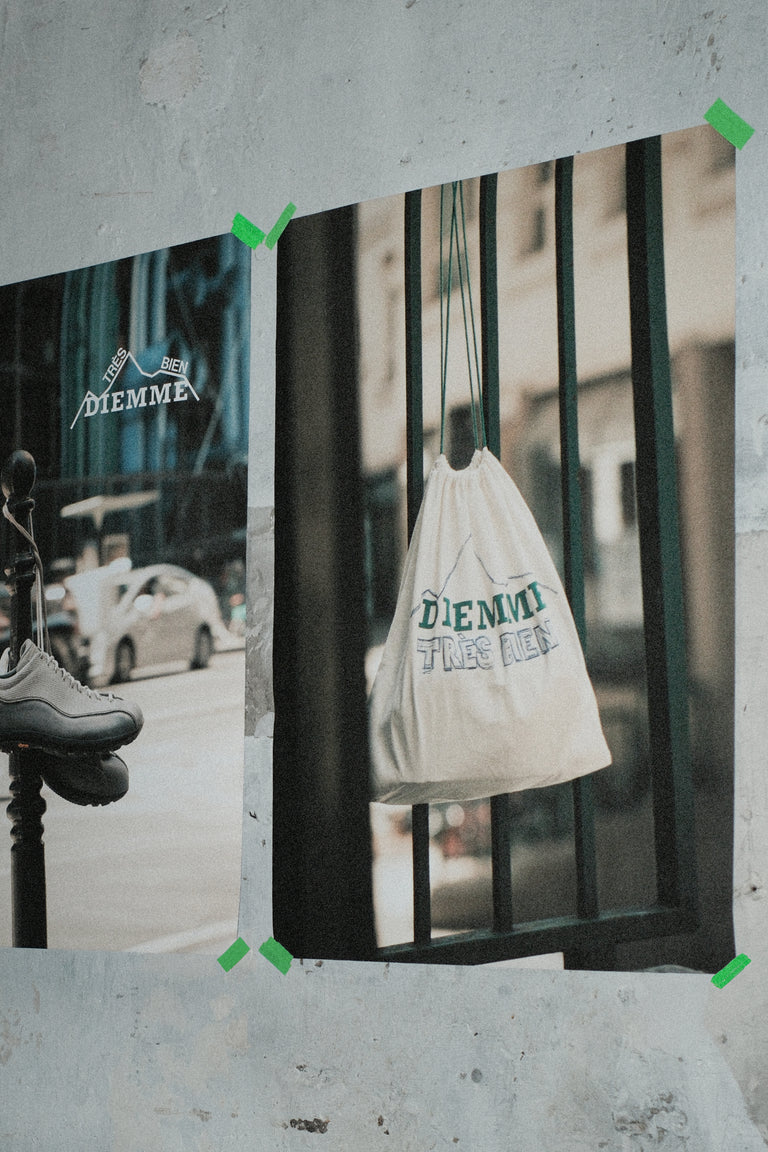 Two taped promotional posters mounted on a concrete wall, showcasing the DIEMME × Très Bien collaboration with a drawstring bag and gray sneakers photographed in urban street set