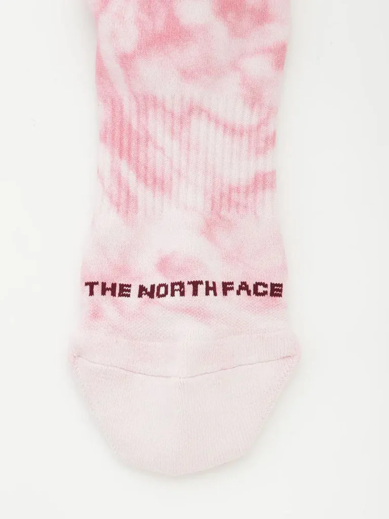 Detailed sock close-up featuring The North Face logo woven into a soft pink tie-dye pattern with cushioned knit construction