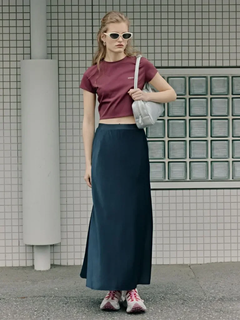 Full-body styling image featuring The North Face VECTIV Breeze sneakers worn with a burgundy crop top, navy skirt, and sporty accessor