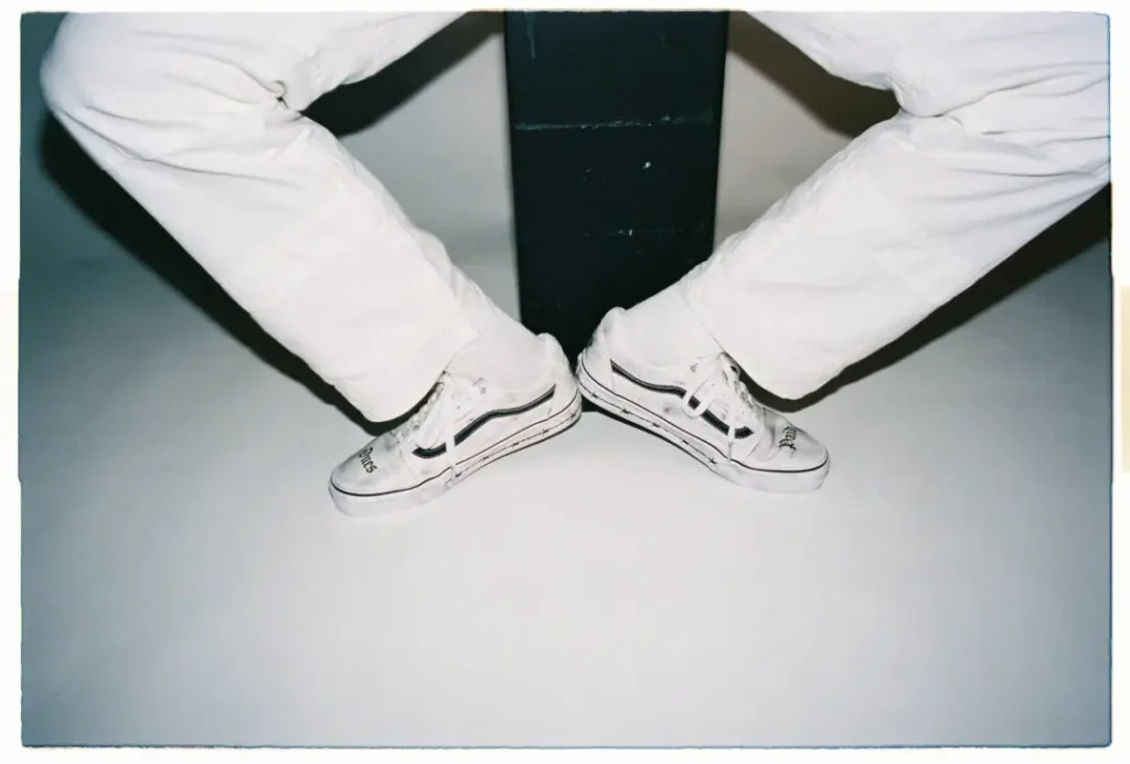 Lifestyle image of two people sitting opposite each other with crossed legs, wearing matching Travis Barker x Vans Old Skool shoe