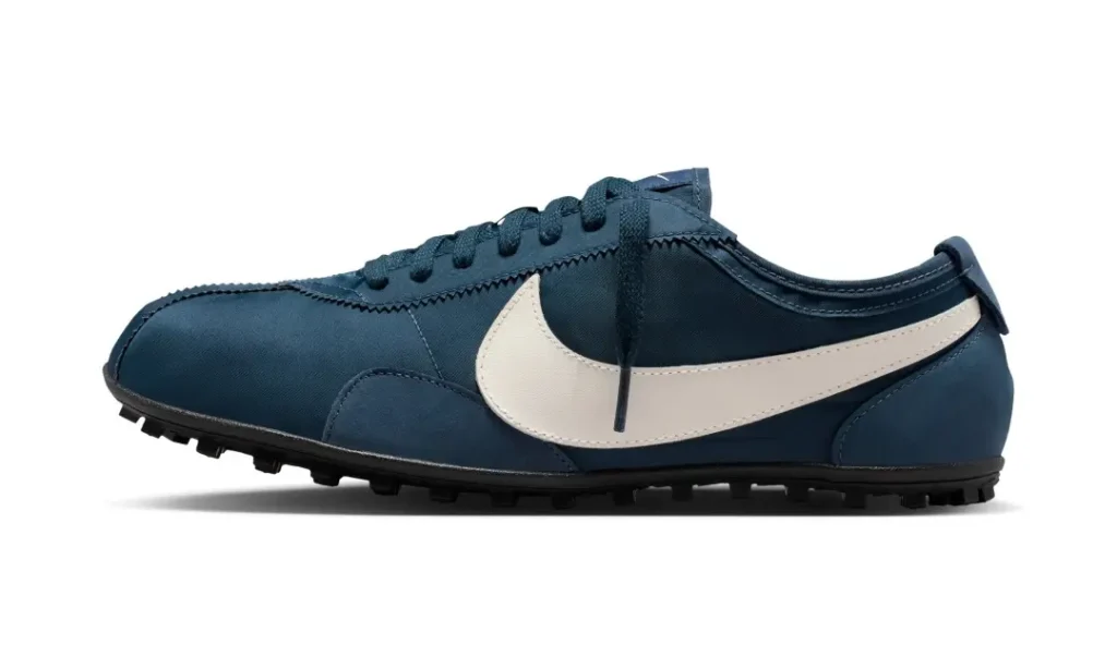 Side profile of a navy blue Nike Cortez-style shoe featuring a large white leather Swoosh, tonal laces, and a low-cut design with trail-inspired traction