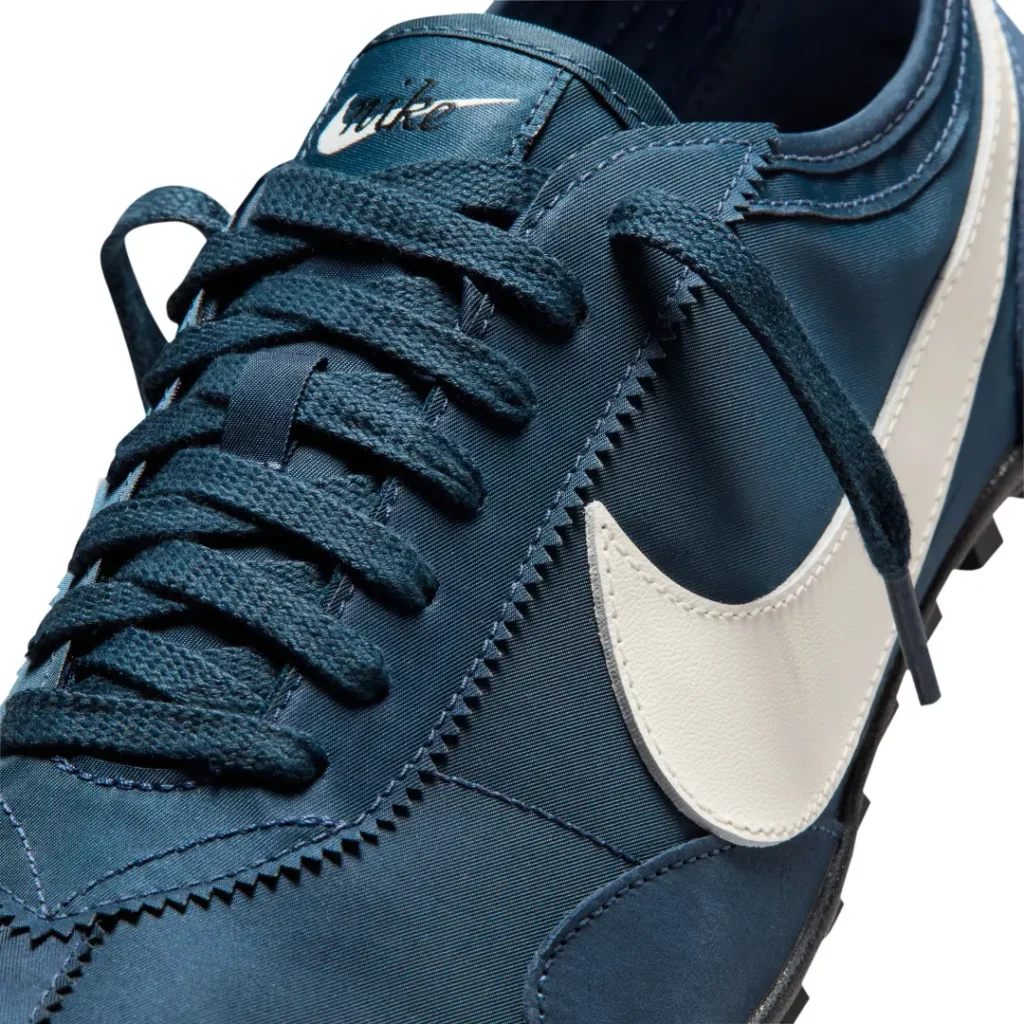 Close-up of the navy nylon upper showing textured flat laces, zigzag-edged eyestays, vintage Nike tongue branding, and the oversized white Swoosh
